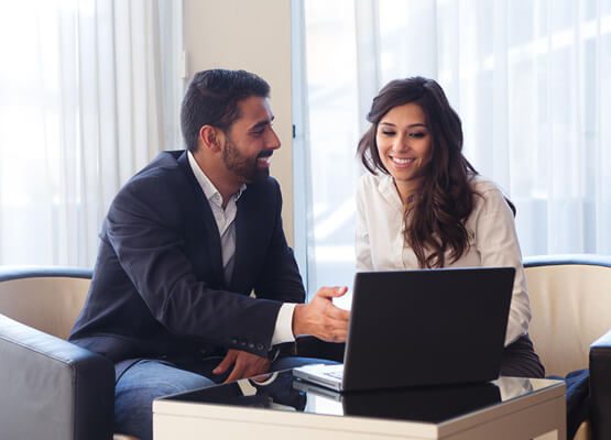 Two professionals in business attire engaged in a focused discussion over a laptop, symbolizing high-level business consulting and strategic advisory services.