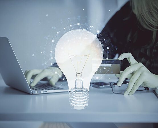 A hand reaching out to touch a glowing lightbulb emerging from a laptop screen, symbolizing the innovative digital solution and the breakthrough technology delivered for the marketplace.