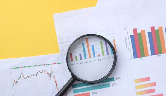 A magnifying glass held over a business chart showing growth trends and data, symbolizing in-depth market research, data analysis, and strategic discovery.
