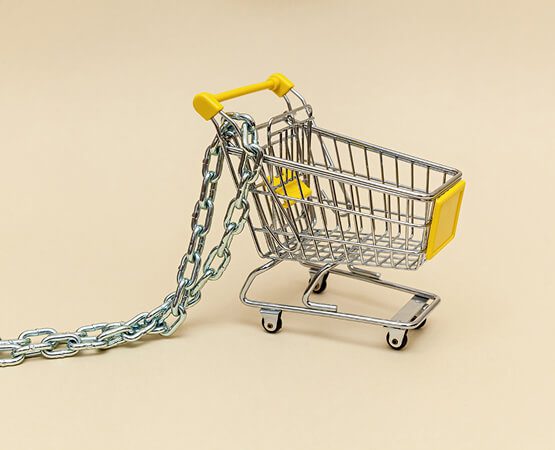 A miniature shopping cart tethered by a heavy metal chain, symbolizing the business challenge of limited scalability, complex logistics, and difficulty in connecting small, independent high street shops to a broader audience.