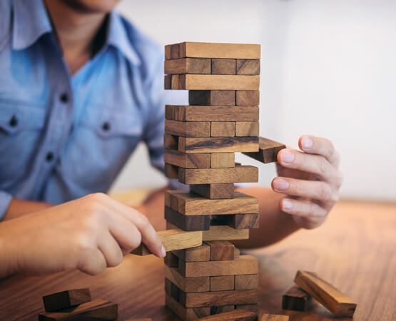 Two people carefully pulling a block from a Jenga tower, symbolizing the delicate balance, risk, and complex management challenges in high-stakes consulting engineering projects.