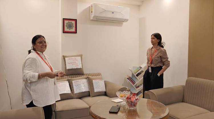 Srishti & Madhu Verma in the office lounge area standing near a sofa that has several handwritten activity signs taped to its cushions.