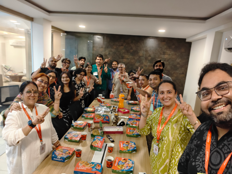 Group of Wisitech employees smiling and making peace signs for a group selfie around a conference table covered with Domino's pizza boxes.
